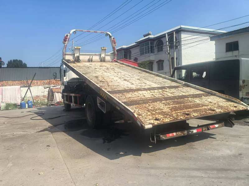 Left view of used Isuzu 3 ton flatbed wrecker truck with deployed flatbed for car towing