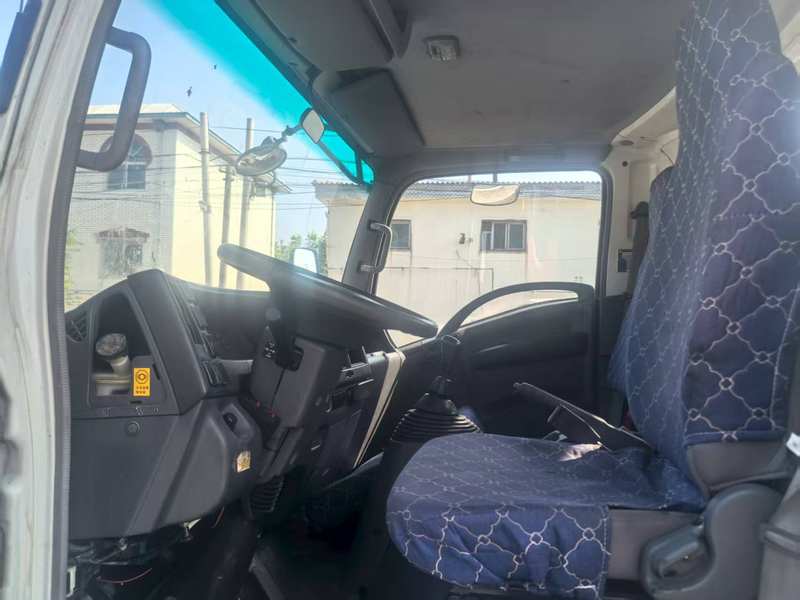 Interior cabin view of Isuzu 3 ton flatbed wrecker tow truck with steering wheel and seat
